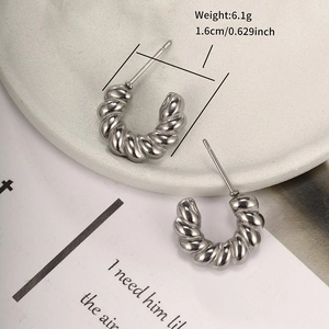 Detail of silver stainless steel C-shaped twisted hoop earrings on white tray