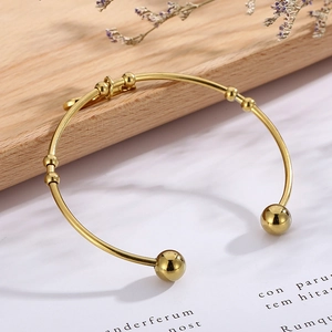 Detailed view of gold-plated violin open bangle with spherical ends on a wooden tray