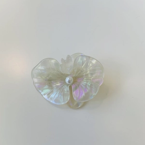Detail of white iridescent floral hair clip with textured petals and center pearl accent