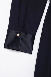 Detailed close-up of dark blue knit sleeve with black satin cuff and gold button accent