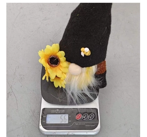 Gnomo di peluche con girasole e ape pesato su una bilancia digitale per mostrare il peso