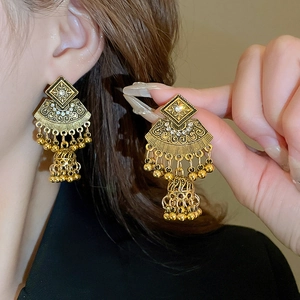 Detail of ethnic golden fan-shaped earrings with intricate carvings and dangling bells