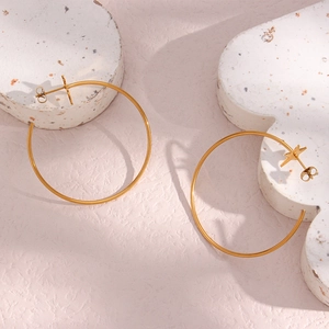Detailed view of gold stainless steel hoop earrings with star charms on marble texture