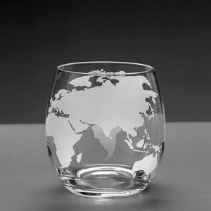 Close-up of clear glass whiskey cup with frosted world map etching and smooth round base