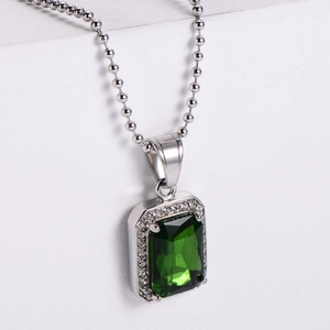 Macro shot of silver hip hop pendant with emerald cut green stone and diamond halo
