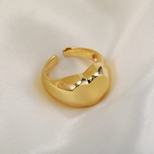 Detailed view of a gold plated heart-shaped open ring resting on white silk fabric