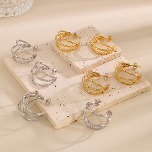 Detailed close-up of layered gold and silver C-shaped titanium earrings with woven textures