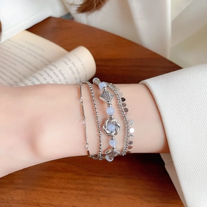 Detail of layered silver bracelets featuring blue crystal beads and vintage swirl charms