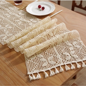 Handmade beige crochet table runner with openwork lace pattern and tassels on wood