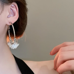 Close-up of model wearing silver round hoop earrings with white 3D flower petal charms