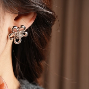 Close-up of a silver hollow flower stud earring with zircon core worn on a model's ear
