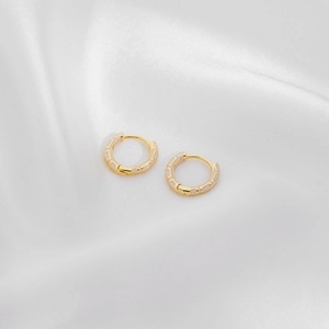 Detailed macro view of gold huggie earrings with white enamel inlay on silk