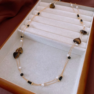 Detail of heart-shaped tiger eye stone and white pearls on a gold layered necklace