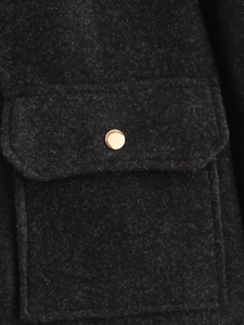 Nahaufnahme der schwarzen Tweed-Textur und des polierten Goldknopfs auf der Tasche