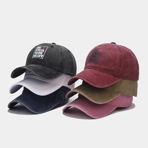 Vertical stack of six washed cotton baseball caps in multiple colors with heart embroidery