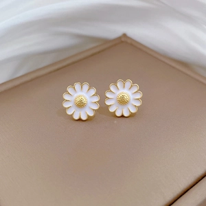 Detailed close-up of daisy stud earrings with white enamel petals and gold plating