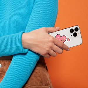 Pink heart sticker with arrow on mobile phone held by hand against orange backdrop