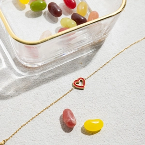 Detail of gold heart pendant with red enamel on a grey marble textured surface