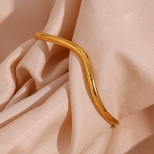 Detailed close-up of a wavy gold stainless steel bracelet on luxurious silk fabric