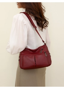 Detail view of burgundy leather shoulder bag with multiple zippers and adjustable strap