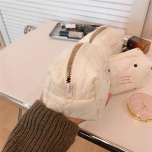 Détail d'une trousse à maquillage en coton matelassé blanc avec fermeture éclair et étiquette