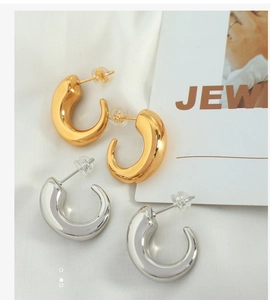 Detailed view of chunky C-shape 18K gold and silver earrings on textured background