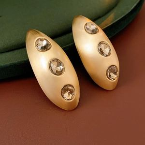 Detail view of oval brushed gold earrings with three inlaid sparkling cubic zirconia