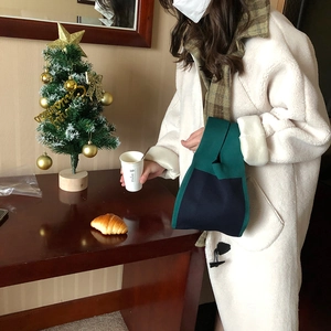 Navy blue and green knitted Japanese knot bag held by a model in a cozy winter scene
