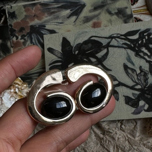 Detail view of artistic gold spiral earrings with oval black resin stone inlay