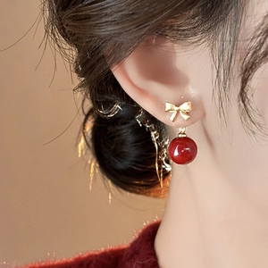 Close-up of golden bow earring with deep red glossy bead on model's ear