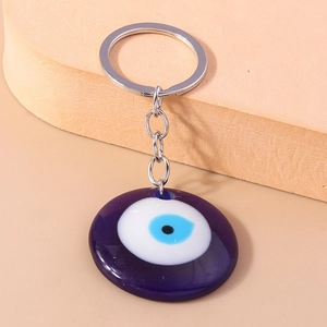 Close-up of a blue Evil Eye keychain with silver-plated ring on a beige textured background