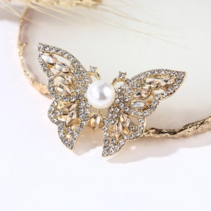 Close-up of golden butterfly brooch with a large white pearl and sparkling rhinestones