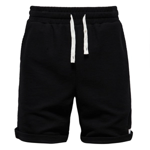 Macro detail of men's black waffle knit shorts showing elastic waist and contrast drawstring