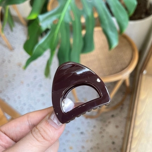 Glossy dark brown triangle hair claw clip for high ponytail styling on a warm background