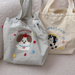 Close-up of wrinkled nylon tote bags featuring puppy embroidery and drawstring details