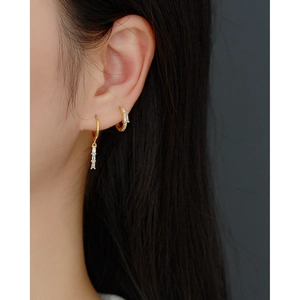 Close-up of elegant gold hoop earrings with rectangular zircon pendants on model's ear