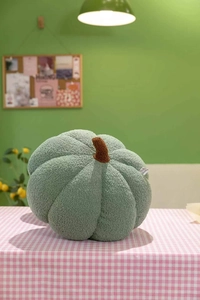 Close-up of green pumpkin plush pillow with brown stem on a checkered tablecloth