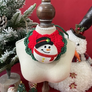 Close-up of knit Christmas pet bib with snowman patch on festive red background