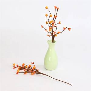 Detailed close-up of realistic artificial orange berry branches in a green ceramic vase