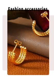 Macro shot of three-layered C-shaped gold-plated steel earrings on brown leather