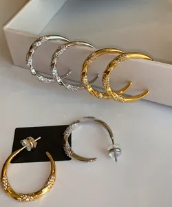 Detail view of twisted C-shaped gold and silver earrings with sparkling cubic zirconia