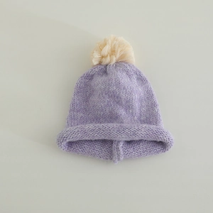 Detail of lavender knitted hat showing soft wool texture and a cream faux fur pom-pom