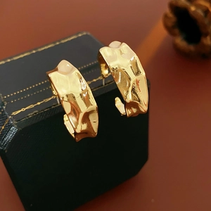 Detailed view of chunky gold-colored C-shaped metal hoop earrings with hammered texture