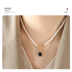 Close-up of pearl necklace with OT clasp and black gemstone pendant on a khaki blazer