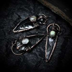Detail of three bronze obsidian arrow pendants featuring iridescent labradorite inlays