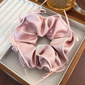Pink silk scrunchie with ribbons displayed in a wooden jewelry tray for a soft aesthetic