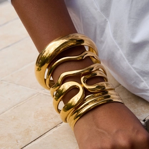 Close-up of stacked gold stainless steel wave bracelets on model's wrist with stone backdrop