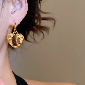 Close-up of golden heart earrings with tiger eye stones and zircon on a female model