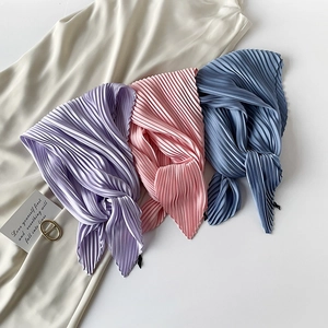 Close-up of pleated silk scarves in purple, pink, and blue on a minimal white surface
