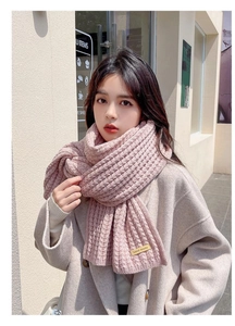 Detail of pink knitted scarf featuring a handmade leather tag and thick ribbed texture